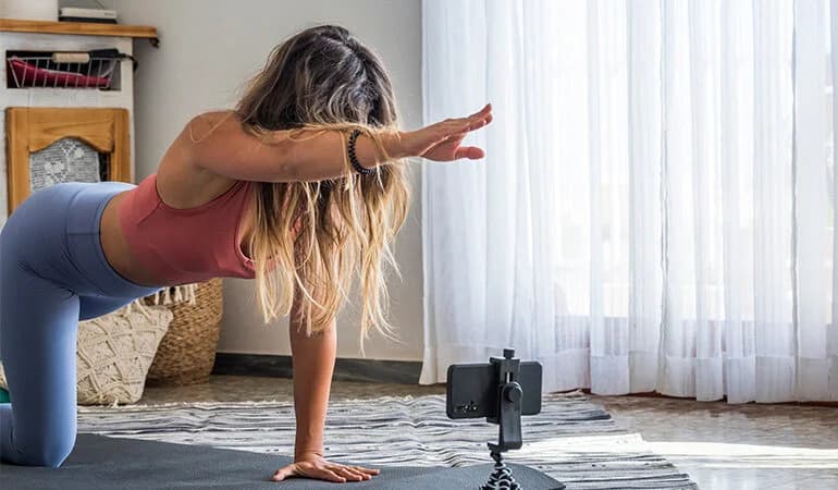 Evde yoga ve egzersiz yapan bir kadın, telefonundaki fitness uygulamasıyla antrenman yapıyor.